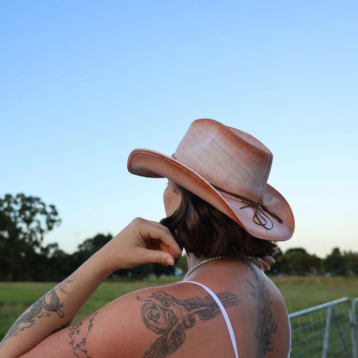Person wearing a straw cowboy hat with tattoos on a grassy field
