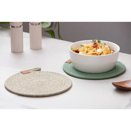 Nash Green Set of 2 Trivets. Bowl of spaghetti on a green coaster with a woven trivet on a white surface.