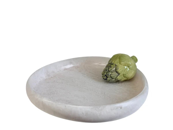 A round, shallow white stone tray with a small green artichoke placed on its rim, photographed against a plain white background.
