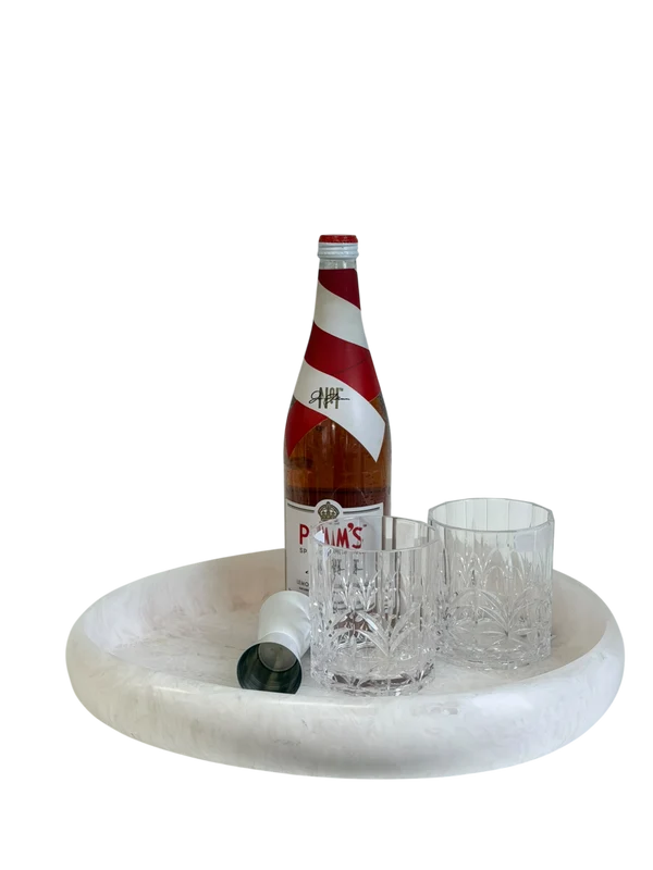 A white oval tray holding a bottle of Palm's soda, two clear cut-crystal glasses, and a small white bottle cap, isolated on a black background.