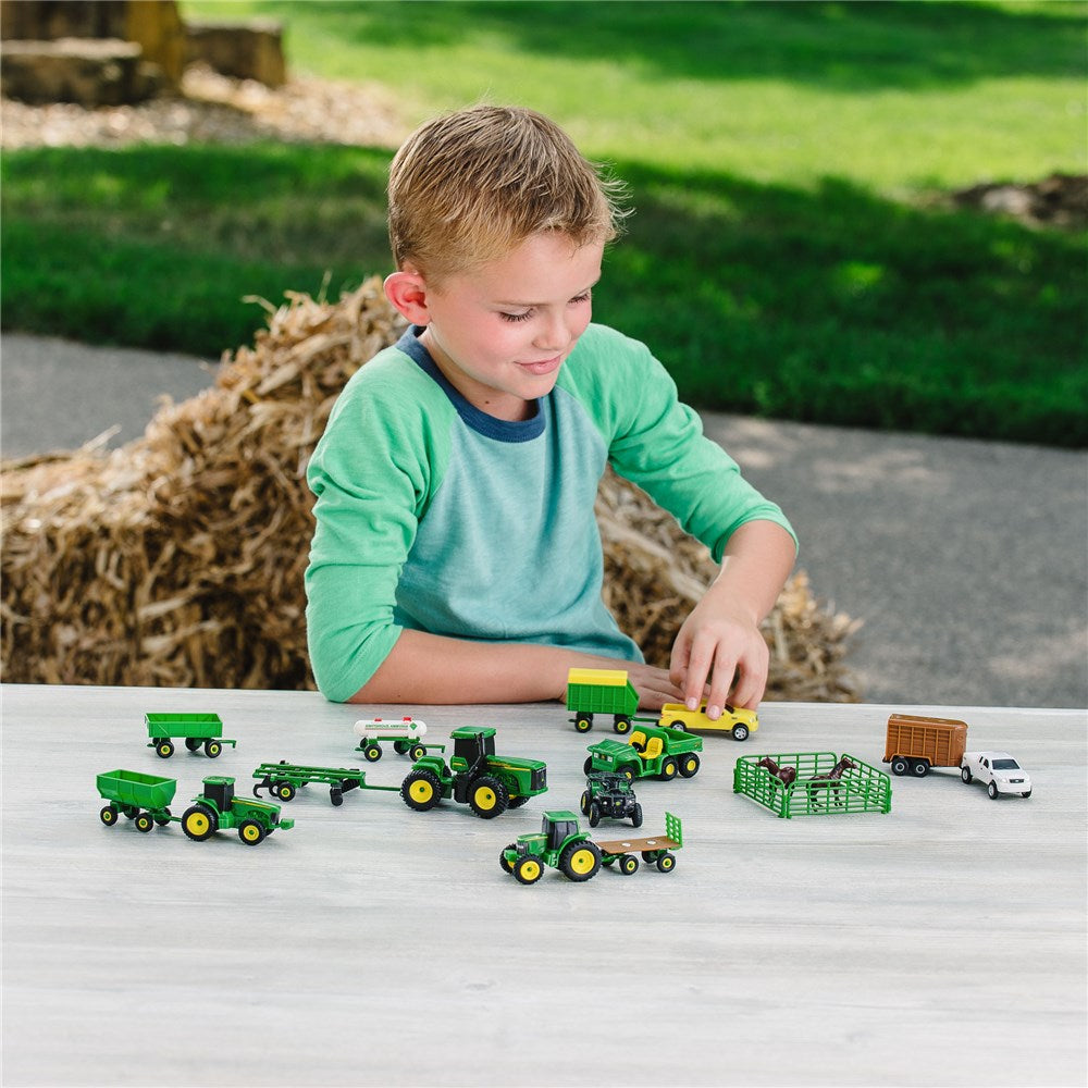 Child playing with toy tractors and trucks on a table outdoors.