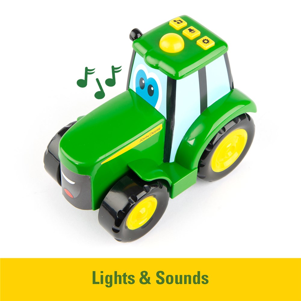 A green toy tractor with yellow wheels and a smiling face, shown on a white background with musical notes and a yellow banner reading 'Lights & Sounds'.