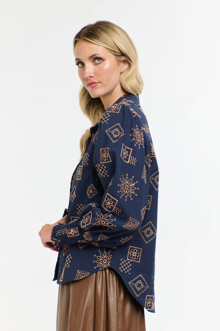 Side view of a woman wearing a 365 Women's Mandala Blouse dark blue patterned blouse with a plain background