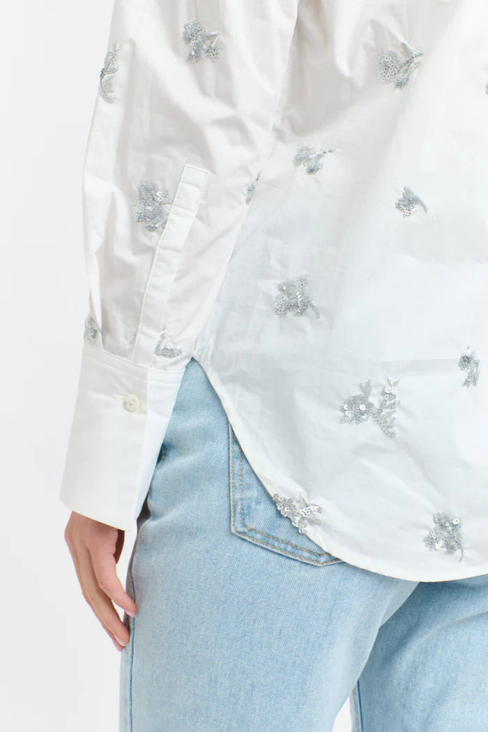 White blouse with floral embroidery worn over light blue jeans on a white background