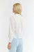 Rear view of a woman wearing a 365 Women's Layla Cotton Top. A white blouse with gold buttons on a white background