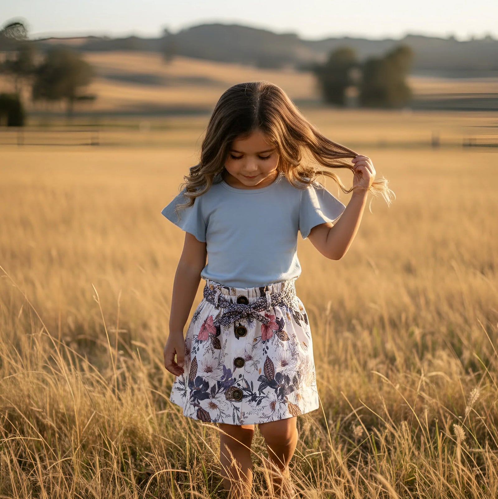 Person wearing a floral skirt and light blue top standing in tall grass.