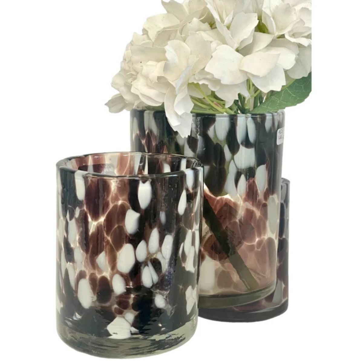 Two clear glass candle holders with a dark brown and white spotted pattern, styled with white flowers on a white background.