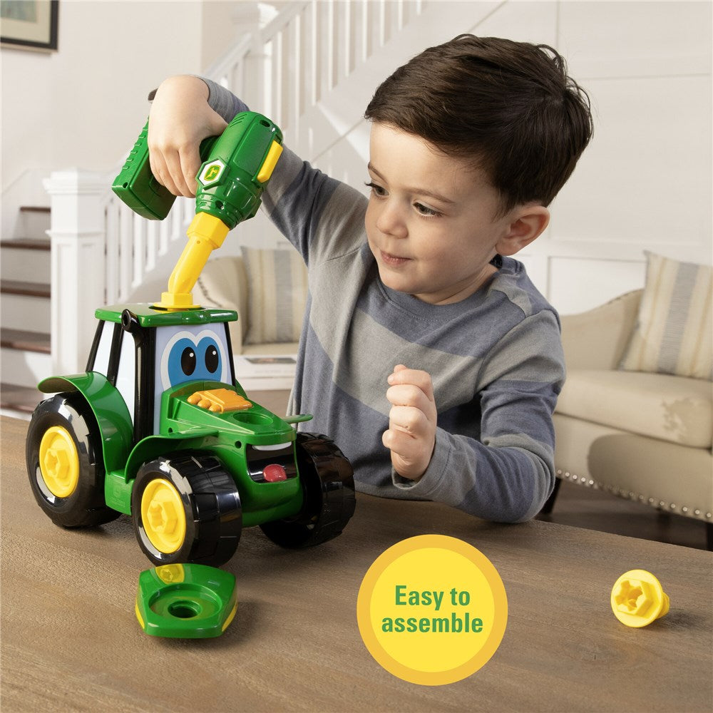 John Deere Build-A-Johnny Tractor. Child playing with a toy drill on a green toy tractor in a living room.