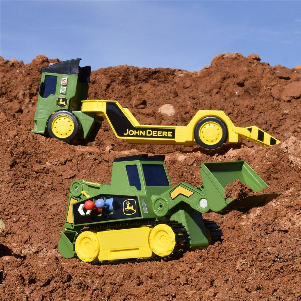 Two John Deere toy construction vehicles, a backhoe loader and a bulldozer, displayed on a pile of brown dirt under a blue sky.