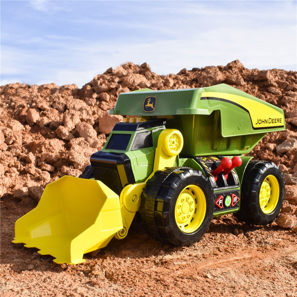 John Deere 46cm Motorised 'Lights & Sounds' 2-n-1 Dig & Dump Rig. Toy dump truck with John Deere logo on a dirt background
