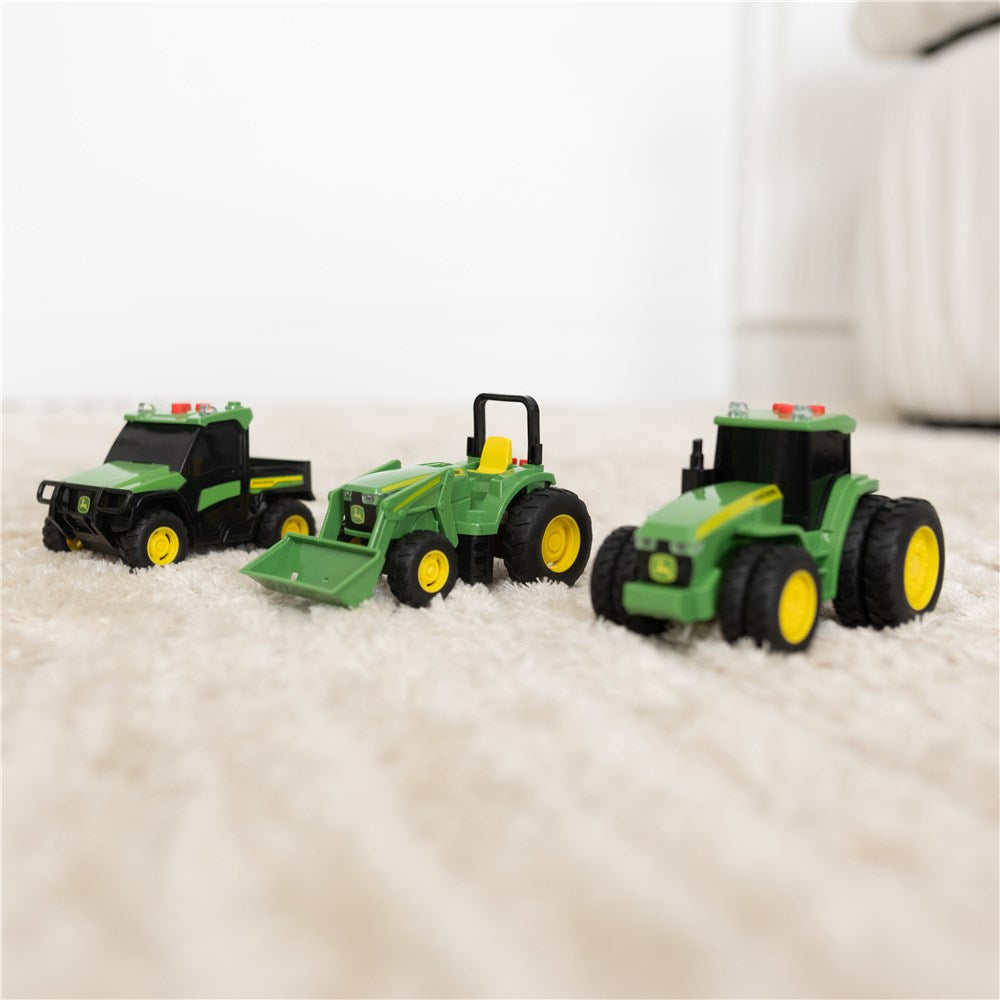 John Deere Lights & Sound Mini Tractors 3-pack. Three toy tractors on a soft surface with a blurred background