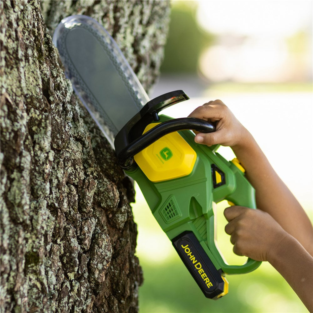 John Deere Motorised Chainsaw. Child's hand holding a John Deere chainsaw against a tree