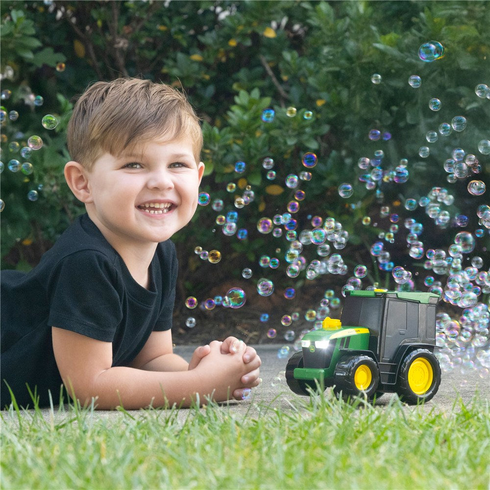 Child playing with a toy tractor in a grassy area with bubbles