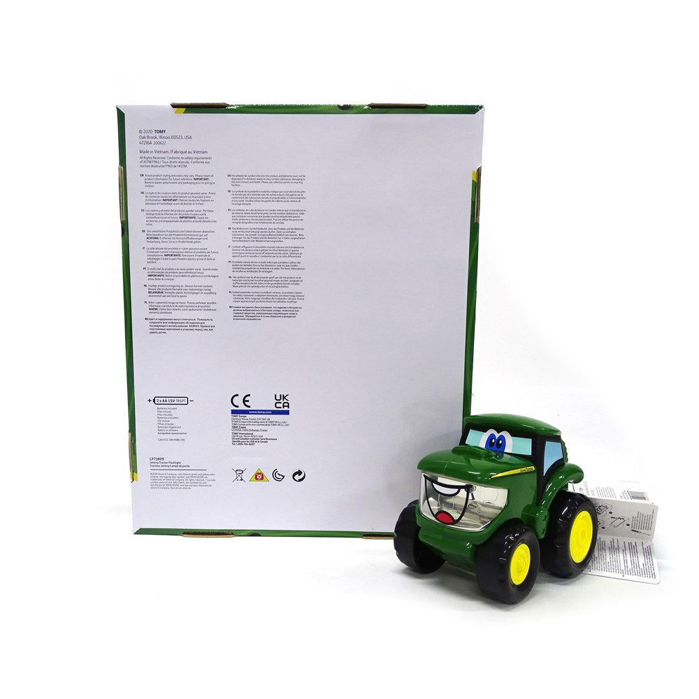 A green toy tractor with yellow wheels and cartoon eyes, shown next to its white retail box on a white background.