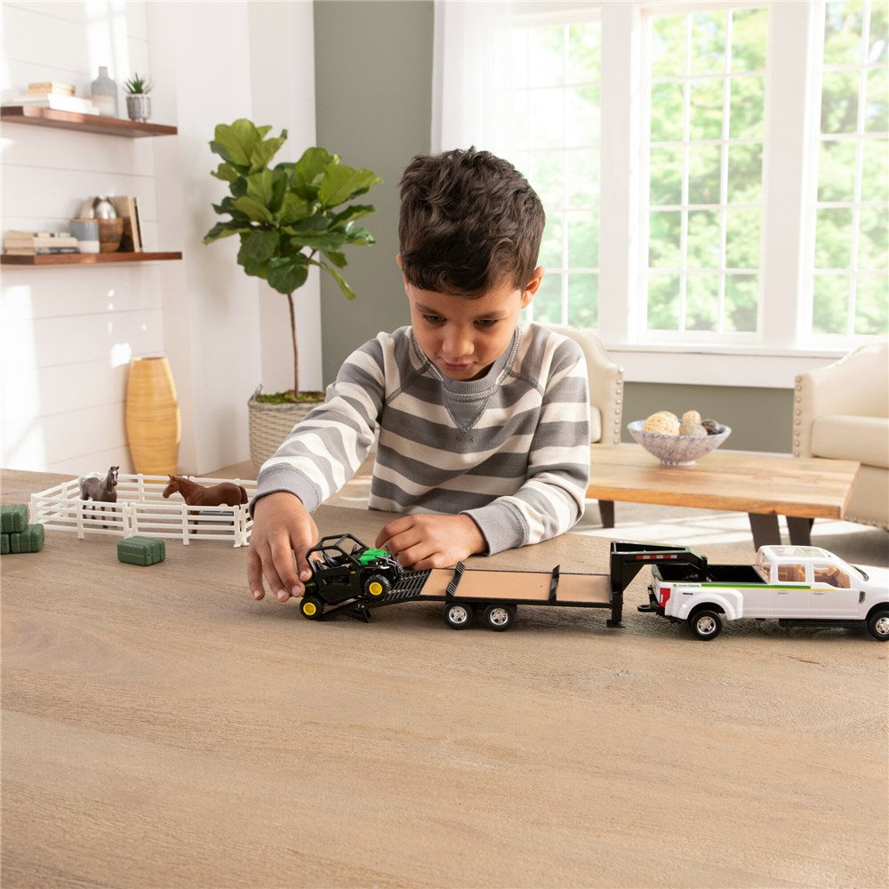 1:32 John Deere RSX860i Gator Hauling Set w/Ford Pickup And Trailer. Child playing with toy trucks on a wooden floor in a bright room.