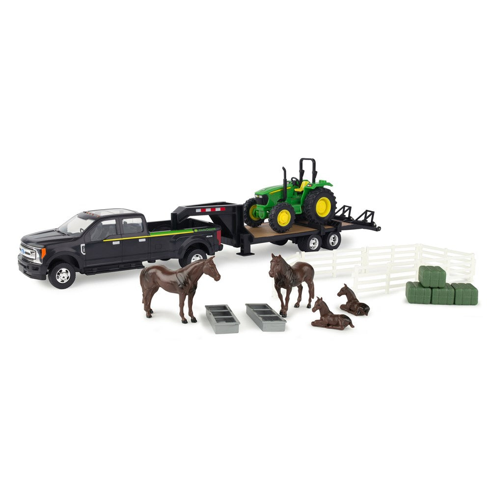 1:32 John Deere 5075E Tractor Hauling Set w/Ford Pickup And Trailer. Toy black pickup truck with trailer carrying a green tractor, surrounded by toy horses and other farm items on a white background.