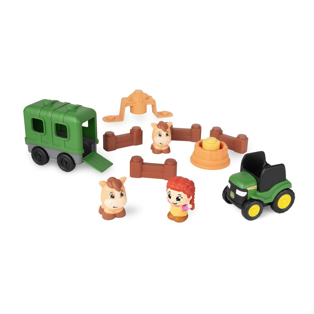 Toy set with a green horse trailer, toy figures of a girl and horses, and small fences on a white background.