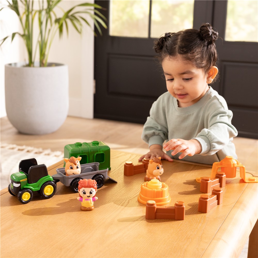 Child playing with toy figures and vehicles on a wooden table.