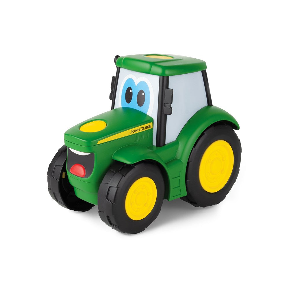A green John Deere toy tractor with cartoon eyes on the windshield, yellow wheels, and a smiling face on the front bumper, shown on a white background.