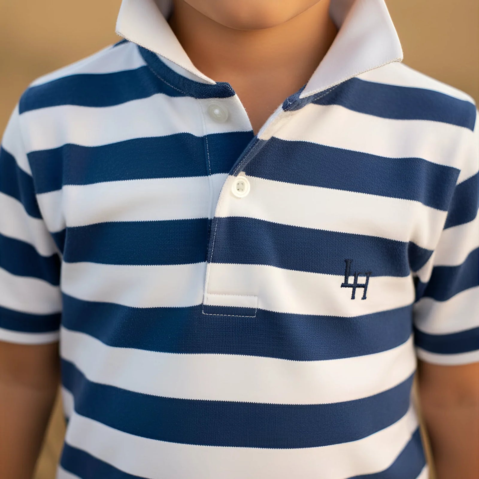 Close-up of a child wearing a blue and white striped polo shirt with a logo on the chest.