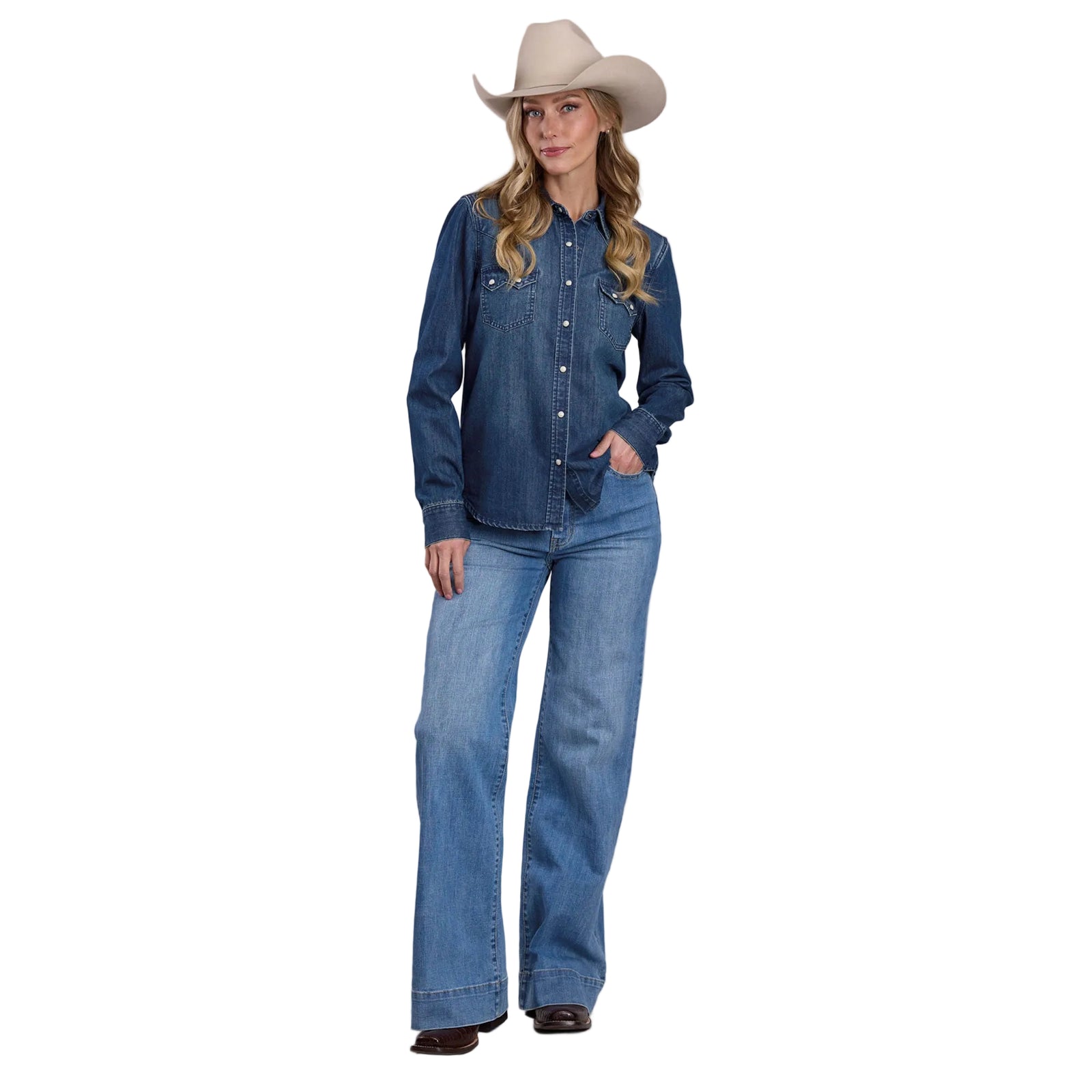Woman wearing a blue denim shirt and jeans with a cowboy hat on a plain background