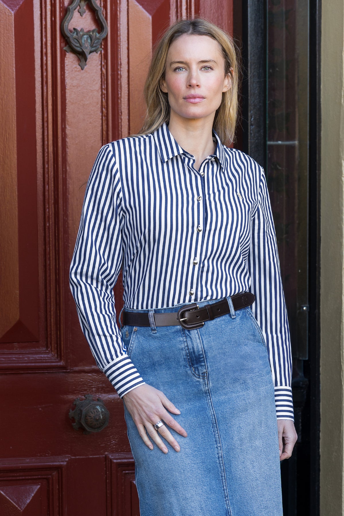 Woman wearing a striped shirt and jeans standing in front of a red door.