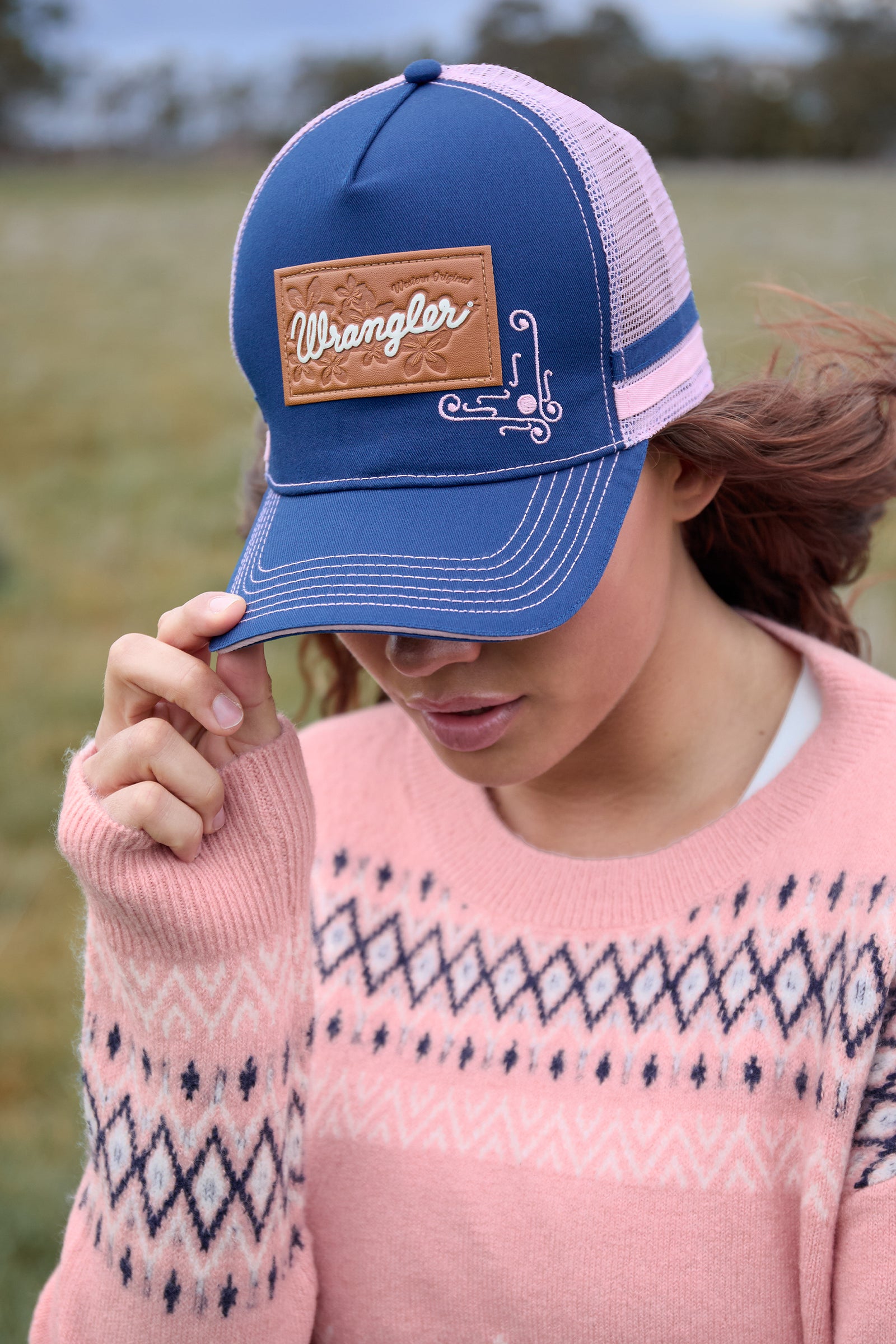 Person wearing a blue cap with a Wrangler logo in an outdoor setting