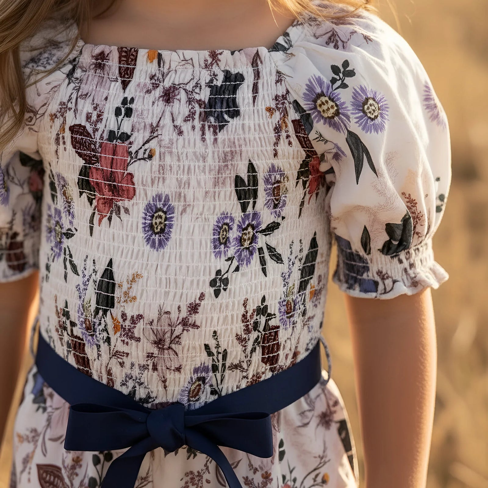 Young girl in a floral dress standing in a field of tall grass.