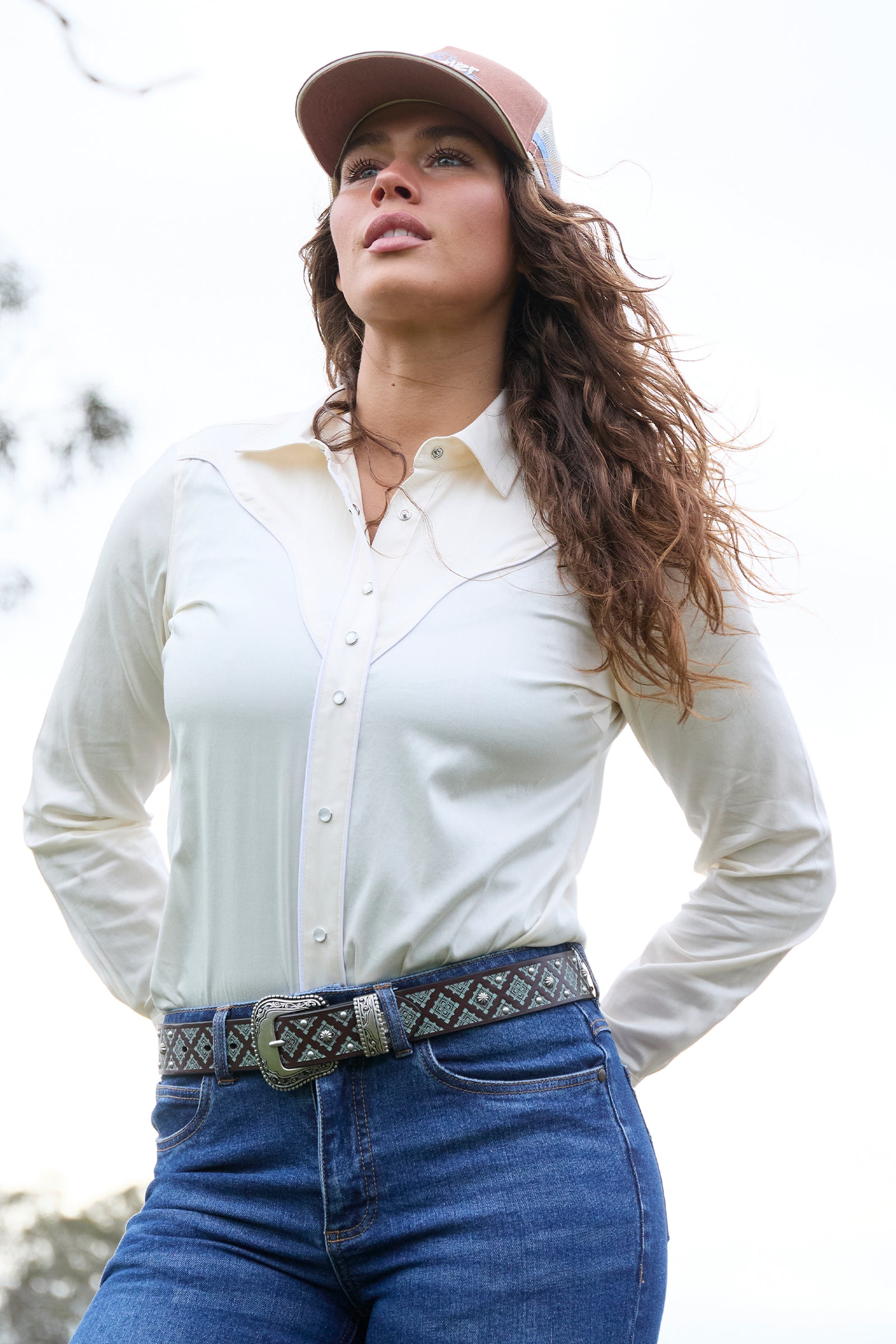 Woman wearing a white shirt, blue jeans, and a pink cap outdoors.