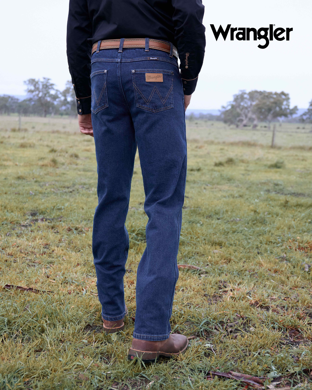 Person wearing blue jeans and a black shirt with 'Wrangler' branding in an outdoor setting.
