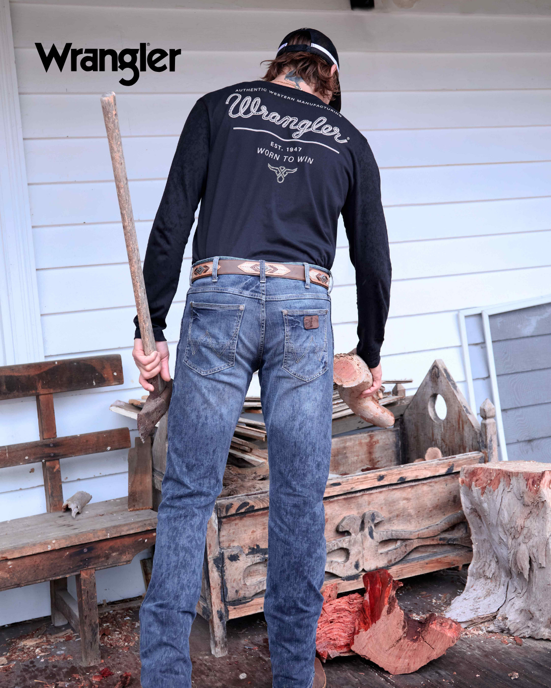 Person wearing a black Wrangler shirt and blue jeans standing on a wooden platform with tools.