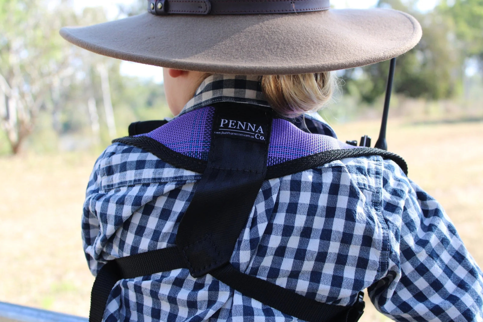 Child wearing a wide-brimmed hat and checkered shirt with a Penna product on a blurred outdoor background