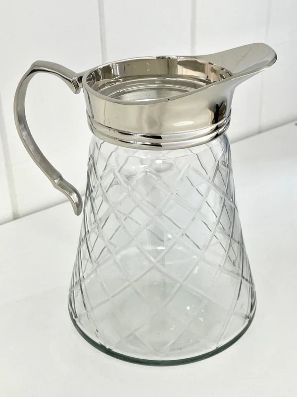 Clear glass pitcher with silver lid and handle on a white background