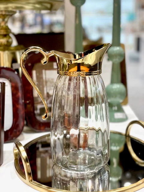 Clear glass pitcher with gold handle and trim on a reflective surface