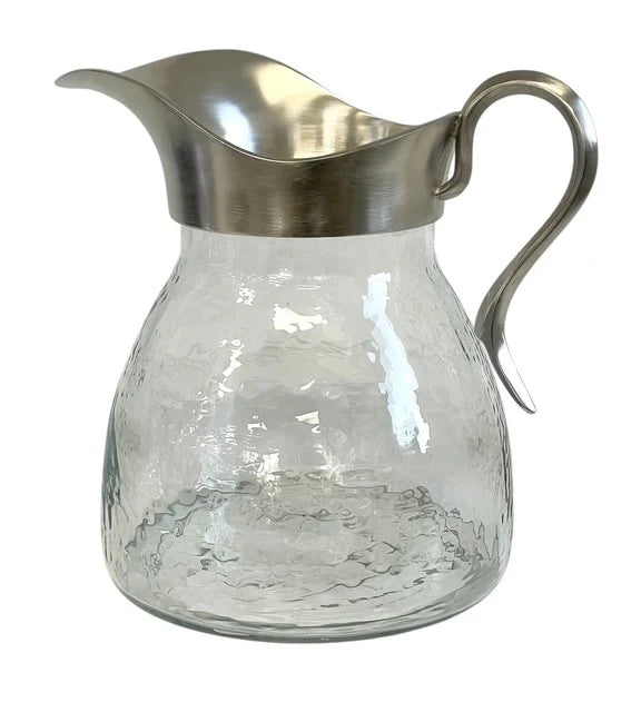 Clear glass pitcher with a silver metal lid and handle on a white background