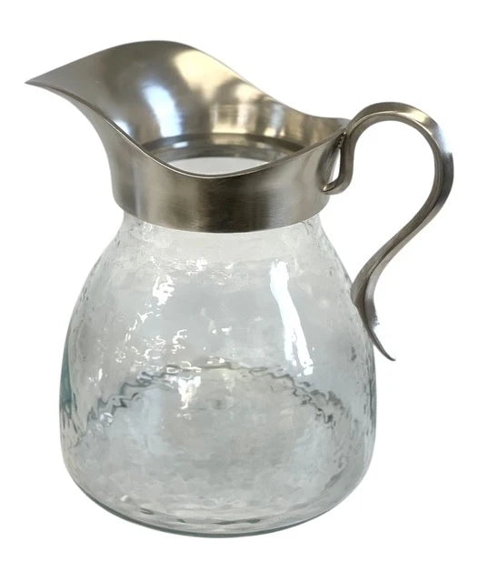 Clear glass pitcher with silver metal lid and handle on a white background