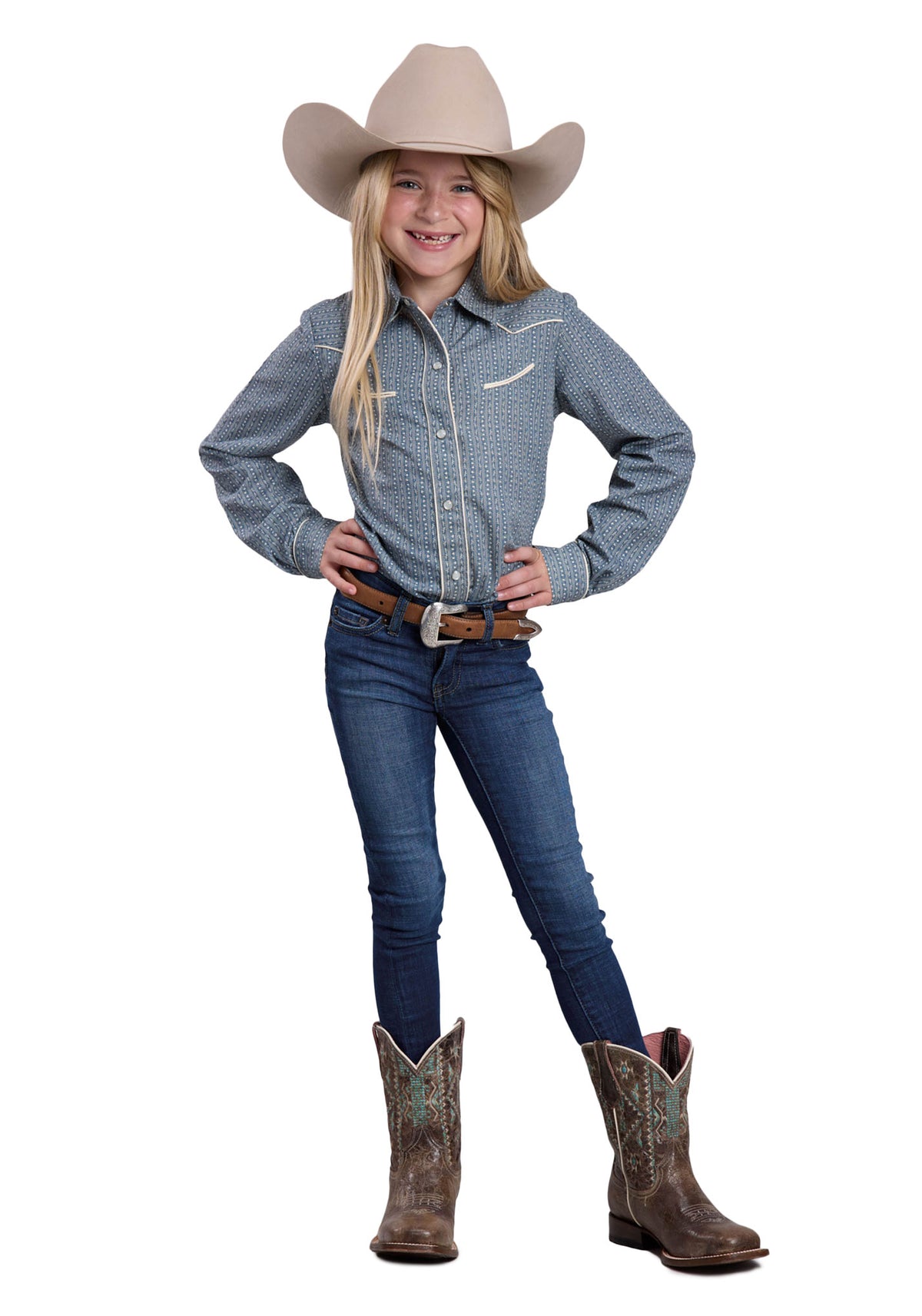 Young girl in cowboy attire with a blue shirt, jeans, and brown boots on a white background