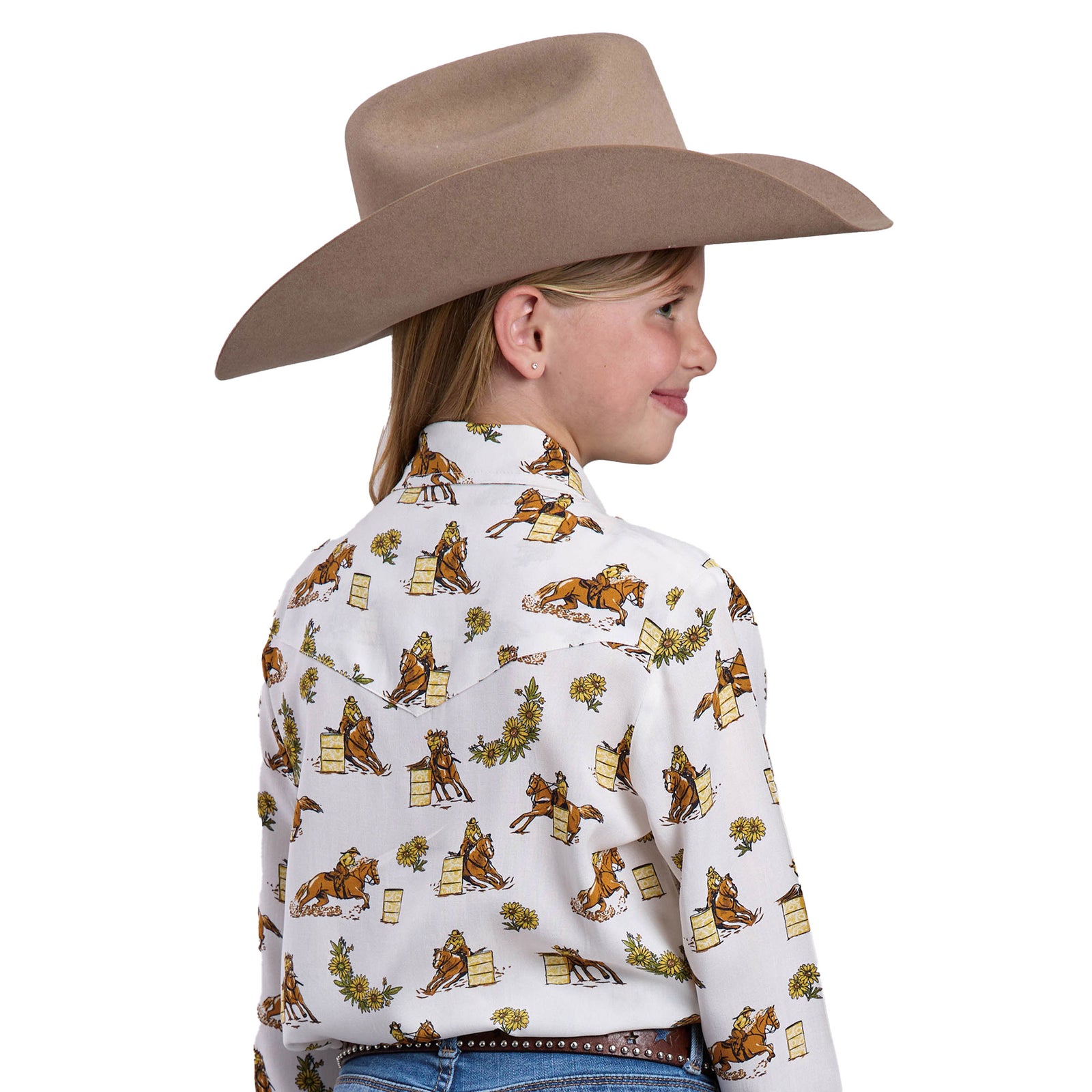 Young girl wearing a white shirt with cowboy print, blue jeans, and a tan cowboy hat on a white background