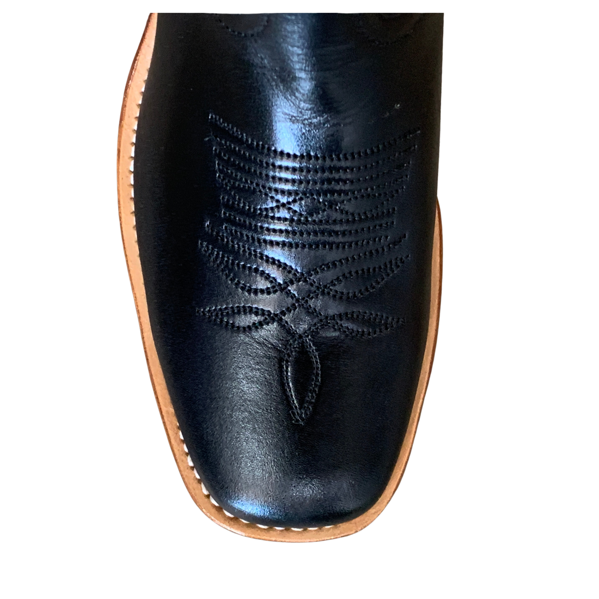 Close-up of a black leather cowboy boot toe showing decorative stitching and a light tan sole edge on a white background.