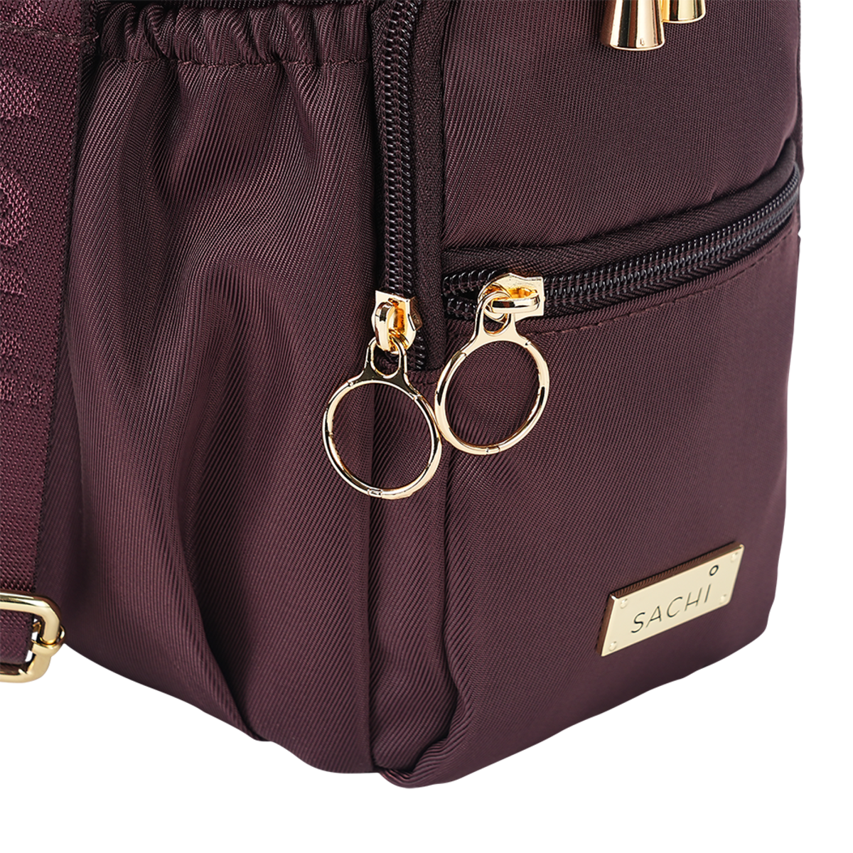 Close-up of a dark plum nylon bag with gold-tone hardware, featuring a drawstring top, a front zip pocket, and a gold brand plaque reading SACHI.