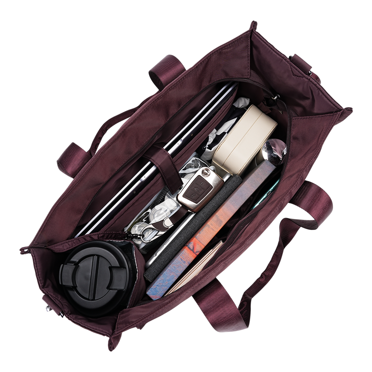A dark plum purple tote bag shown open from a top-down view, packed with various travel accessories including a black insulated tumbler, a beige wallet, a silver watch, and books, isolated on a white background.