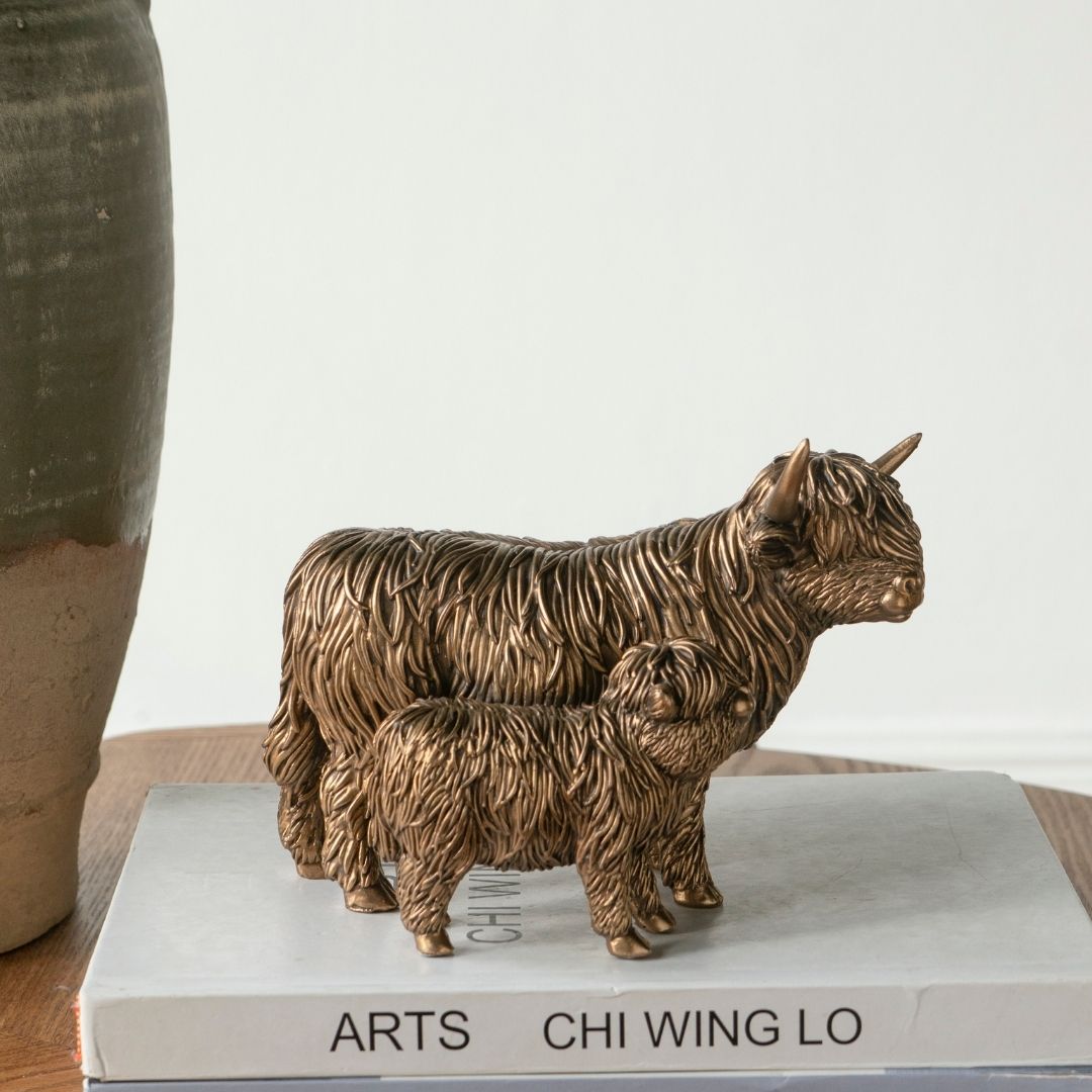 A decorative figurine of a Highland cow and its calf in a textured metallic bronze finish, set against a plain white background.