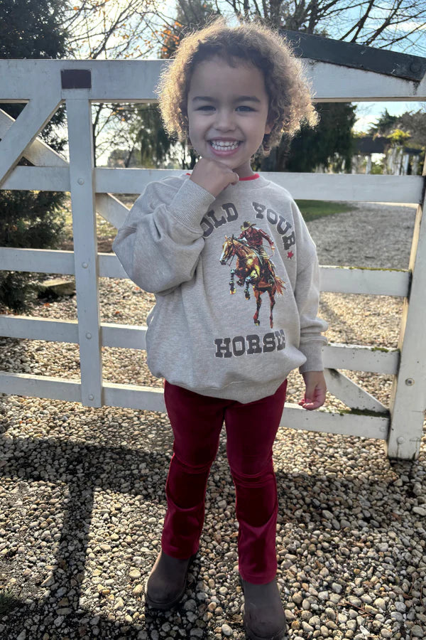 Child wearing a sweatshirt with a horse graphic in front of a white fence.