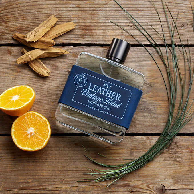 Tru Western Leather Vintage #3 Indigo Blend Label Eau De Cologne 100ml. Perfume bottle with a blue label on a wooden surface with oranges and herbs