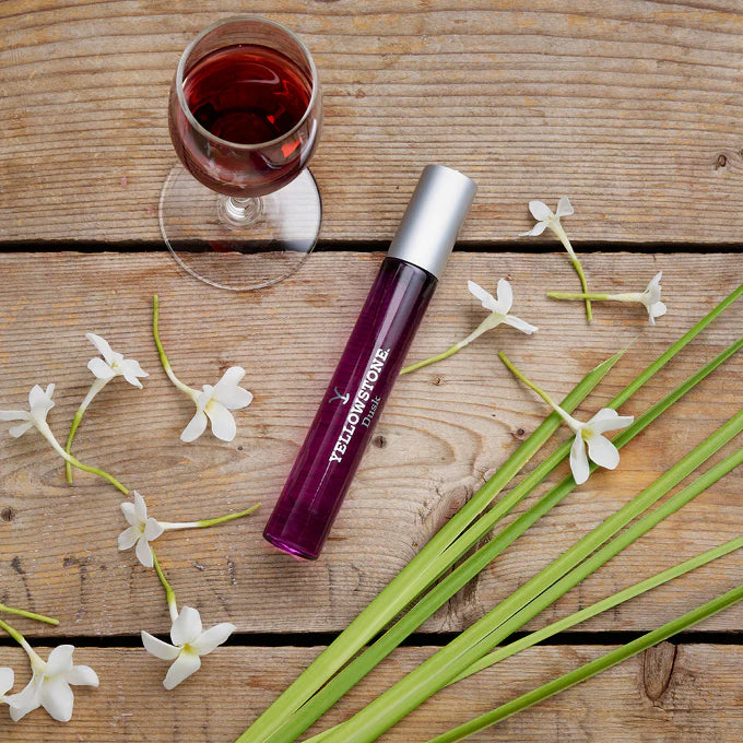 Yellowstone lip balm on a wooden surface with flowers and a glass of red wine.