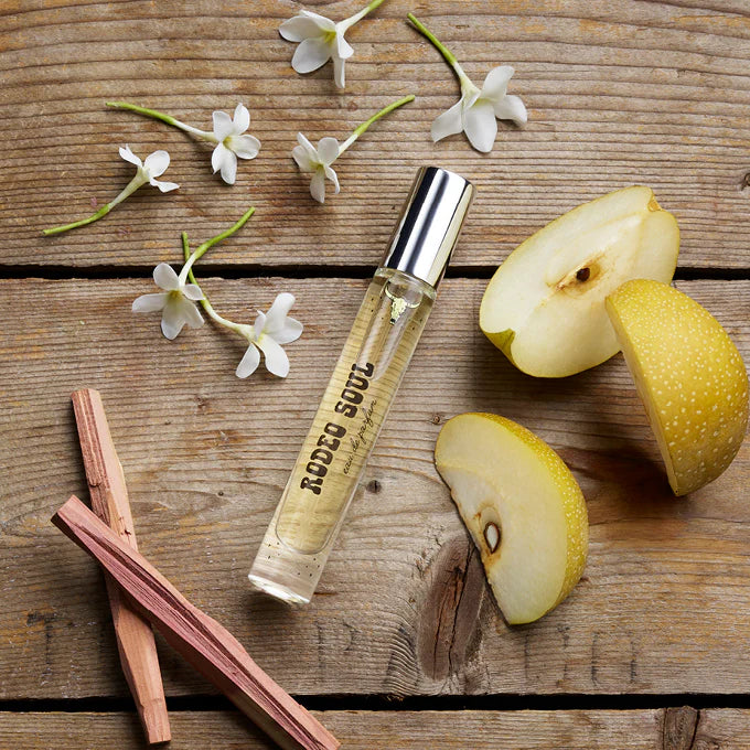 Perfume bottle labeled 'Rodeo Soul' on a wooden surface with pears and flowers.