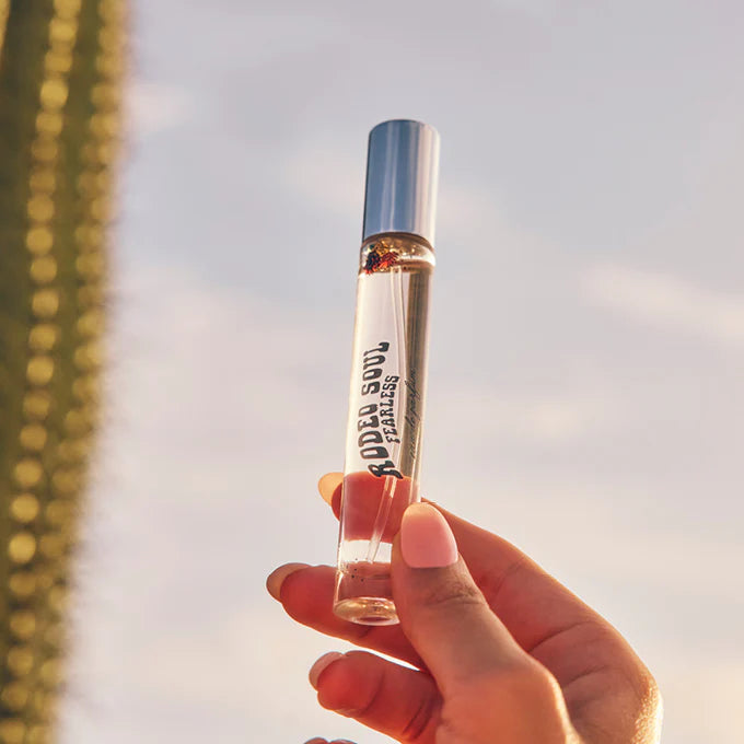 Hand holding a perfume bottle labeled 'RodenSoul' against a blurred natural background