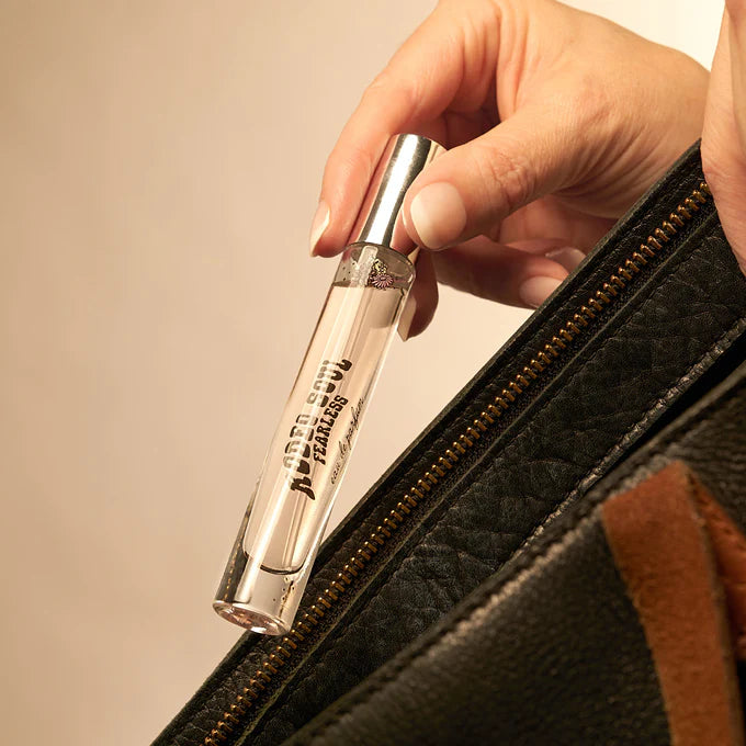 Hand holding a clear cylindrical object with metallic top against a beige background