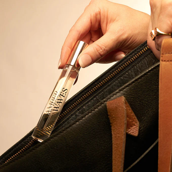 Hand holding a perfume bottle labeled 'Waves' against a beige background