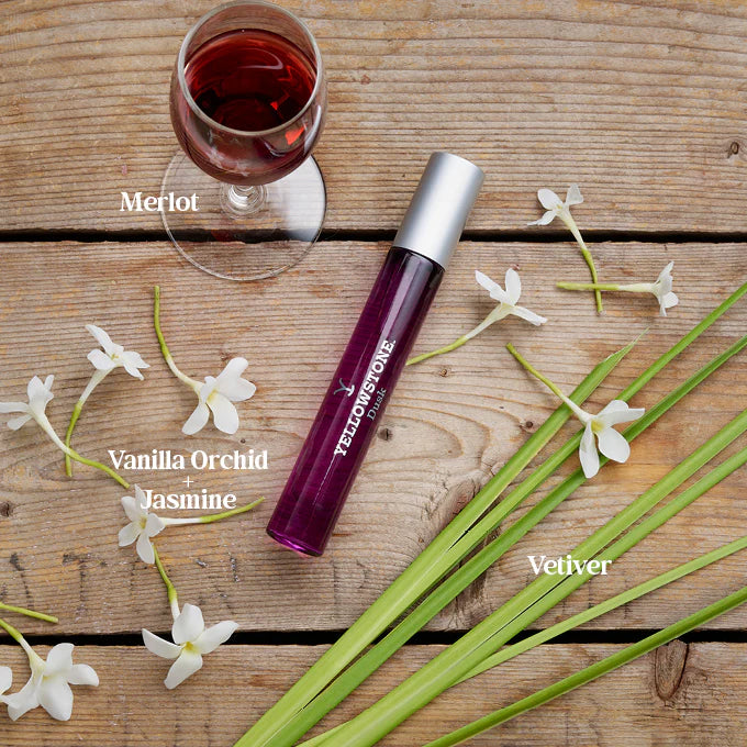 Perfume with floral elements and wine glass on wooden surface